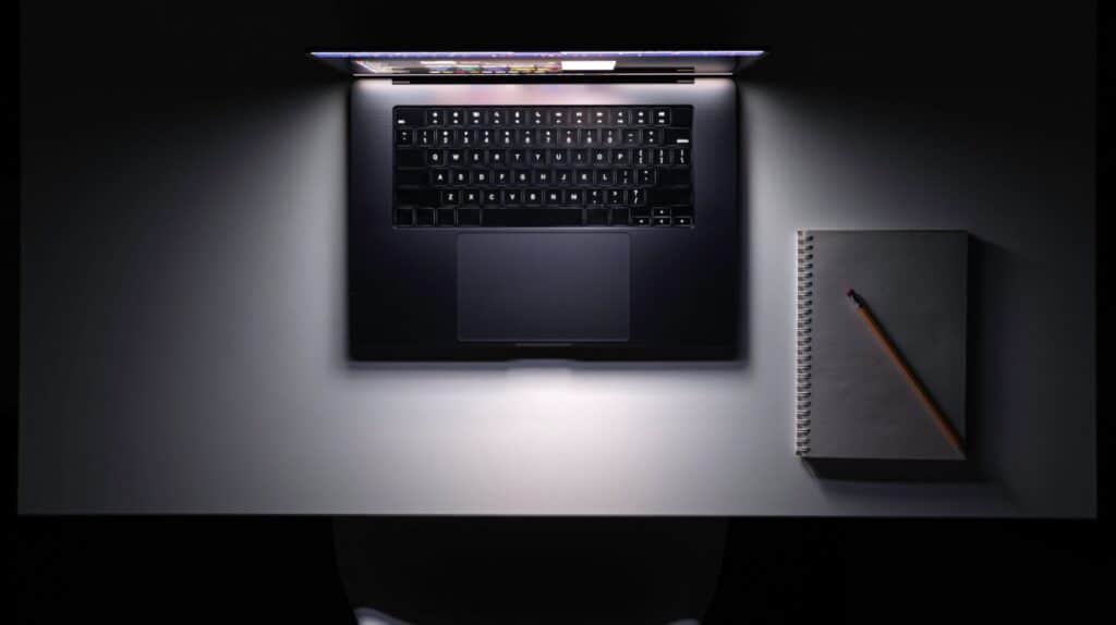 Aufgeklappter Laptop mit Notizbuch von oben auf dunklem Schreibtisch als Symbol fuer Sichtbarkeit in ChatGPT und Google AI Overviews