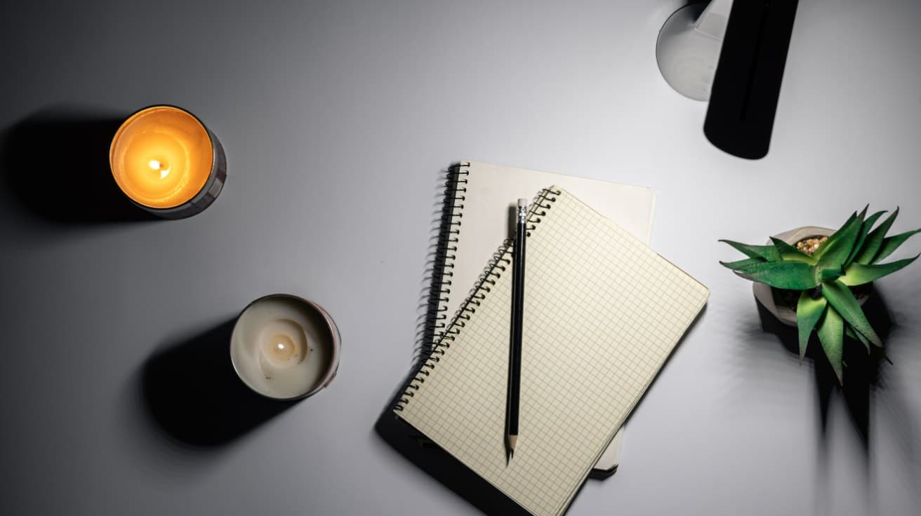 Notizbuch, Stift und Kerze auf einem dunklen Schreibtisch als Sinnbild fürs Website-Texte selbst schreiben