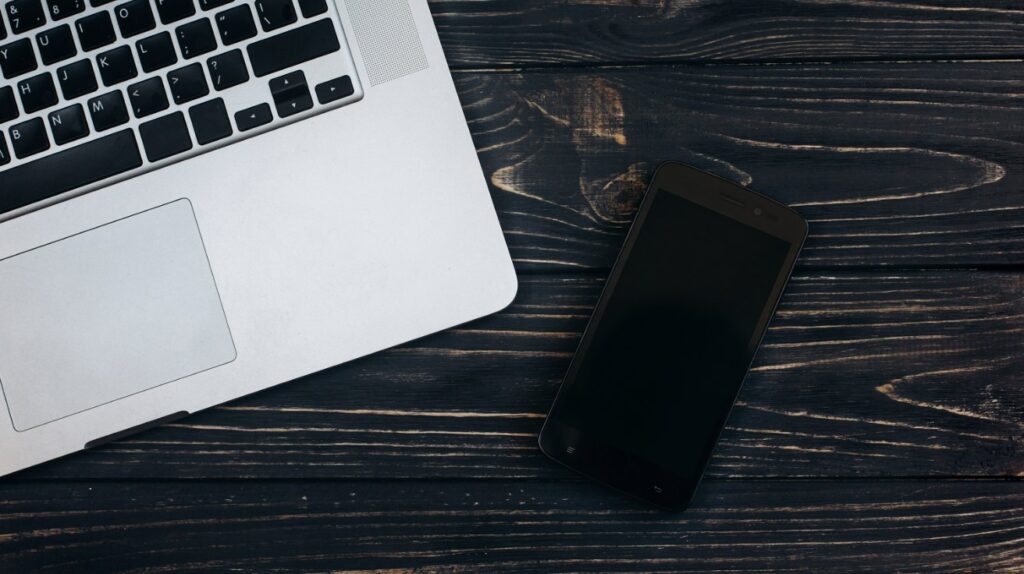 Aufgeklappter Laptop und Smartphone nebeneinander auf einem dunklen Holztisch als Sinnbild für Website und Social Media